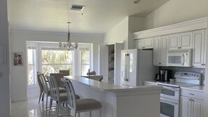 A modern kitchen with white cabinetry, a central island with bar stools, a built-in oven, and a microwave. - STUNNING FRESHLY RENOVATED STONEYBROOK CONDO IN GATED COMMUNITY ON GOLF COURSE (Estero)