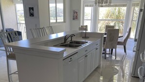 A modern kitchen with a central island, white cabinetry, and a large window providing natural light. - STUNNING FRESHLY RENOVATED STONEYBROOK CONDO IN GATED COMMUNITY ON GOLF COURSE (Estero)