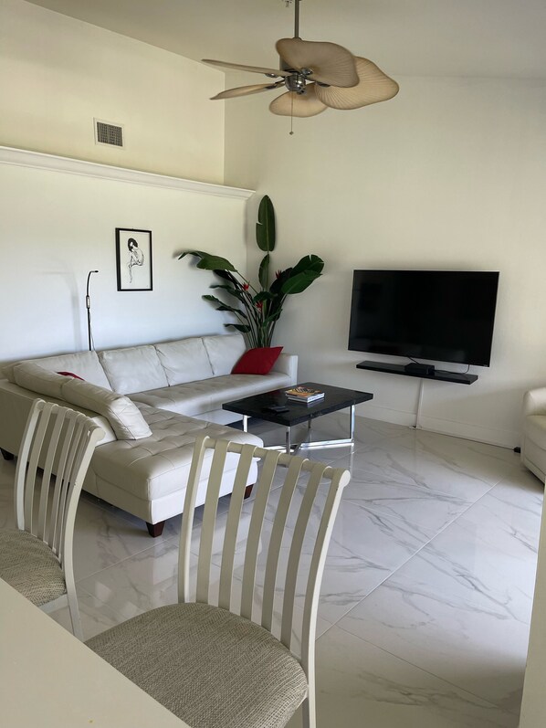 A modern living room with a white sofa, a coffee table, a TV, and a ceiling fan. - STUNNING FRESHLY RENOVATED STONEYBROOK CONDO IN GATED COMMUNITY ON GOLF COURSE (Estero)