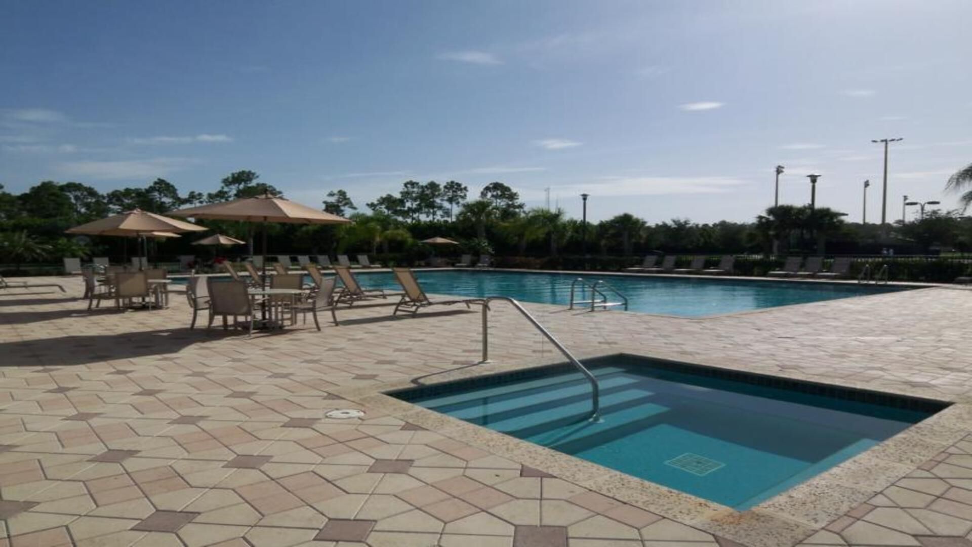 A swimming pool with tiled flooring, lounge chairs, and umbrellas.