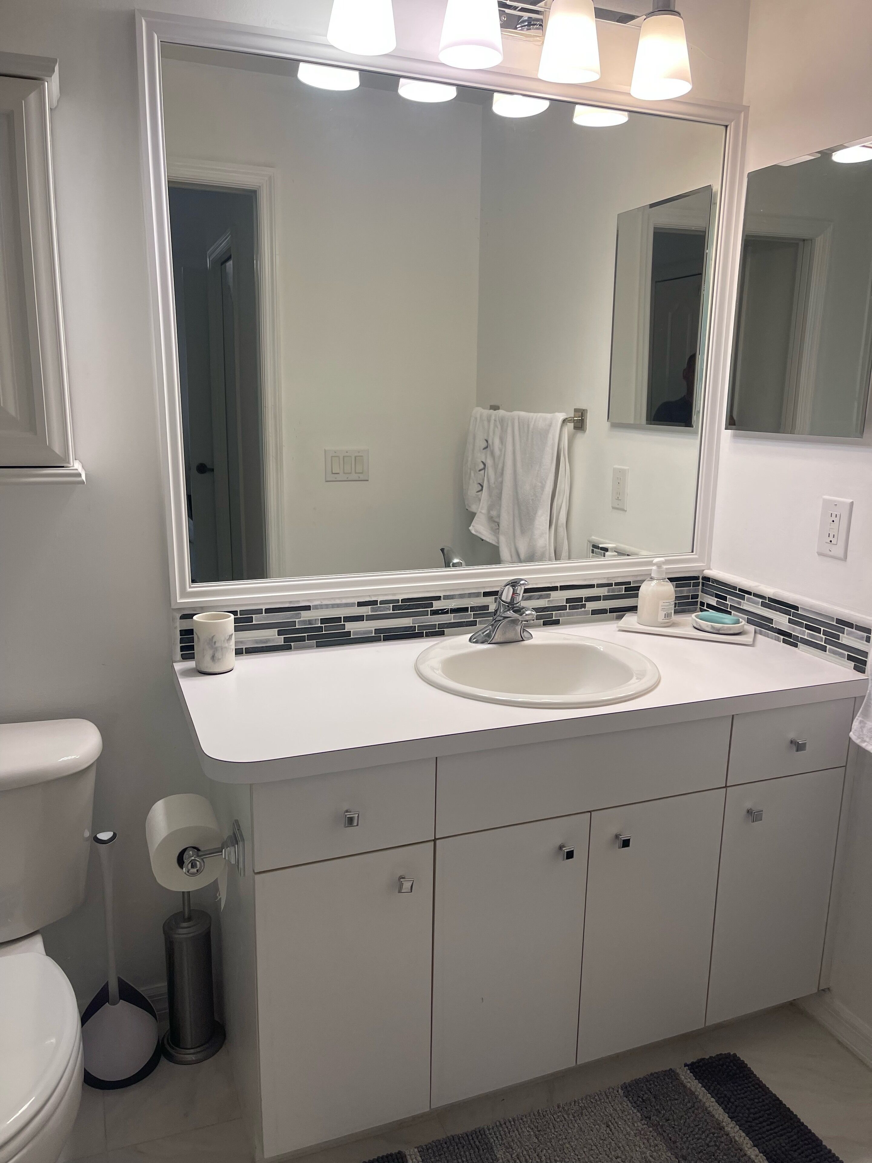 Un baño moderno con un lavamanos blanco, un espejo grande y un salpicadero de azulejos.