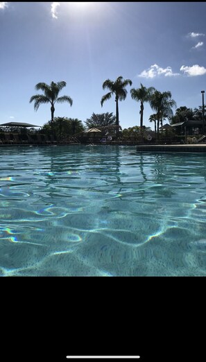 A clear pool with visible water patterns, surrounded by palm trees and a fenced area with lounge chairs. - STUNNING FRESHLY RENOVATED STONEYBROOK CONDO IN GATED COMMUNITY ON GOLF COURSE (Estero)
