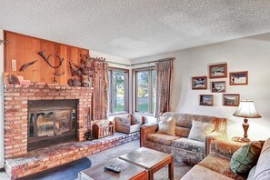 A living room with a brick fireplace, a sofa, a coffee table, and a lamp. - Sunrise 46: Pet Friendly, Mountain Views (Mammoth Lakes)