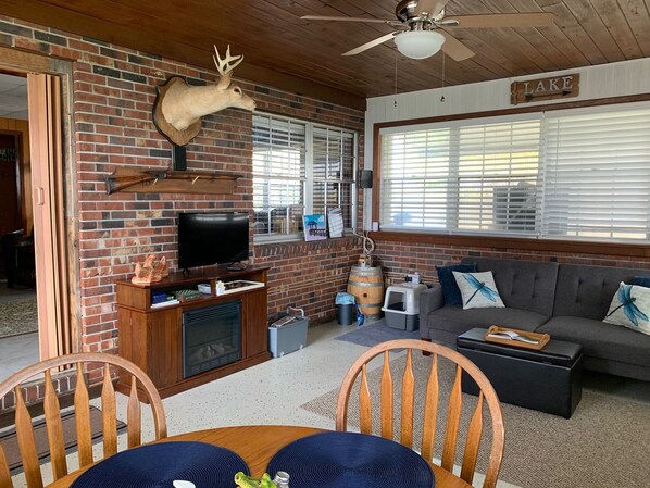 A cozy living room with a brick fireplace, a mounted deer head, a television, and a sofa with decorative pillows.
