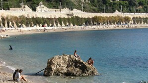 A beach with people sitting on rocks and the sea. - Panoramic seaview terrace overlooking Villefranche/Mer Old Town 10min walk Beach (Provence-Alpes-Côte-D’Azur)