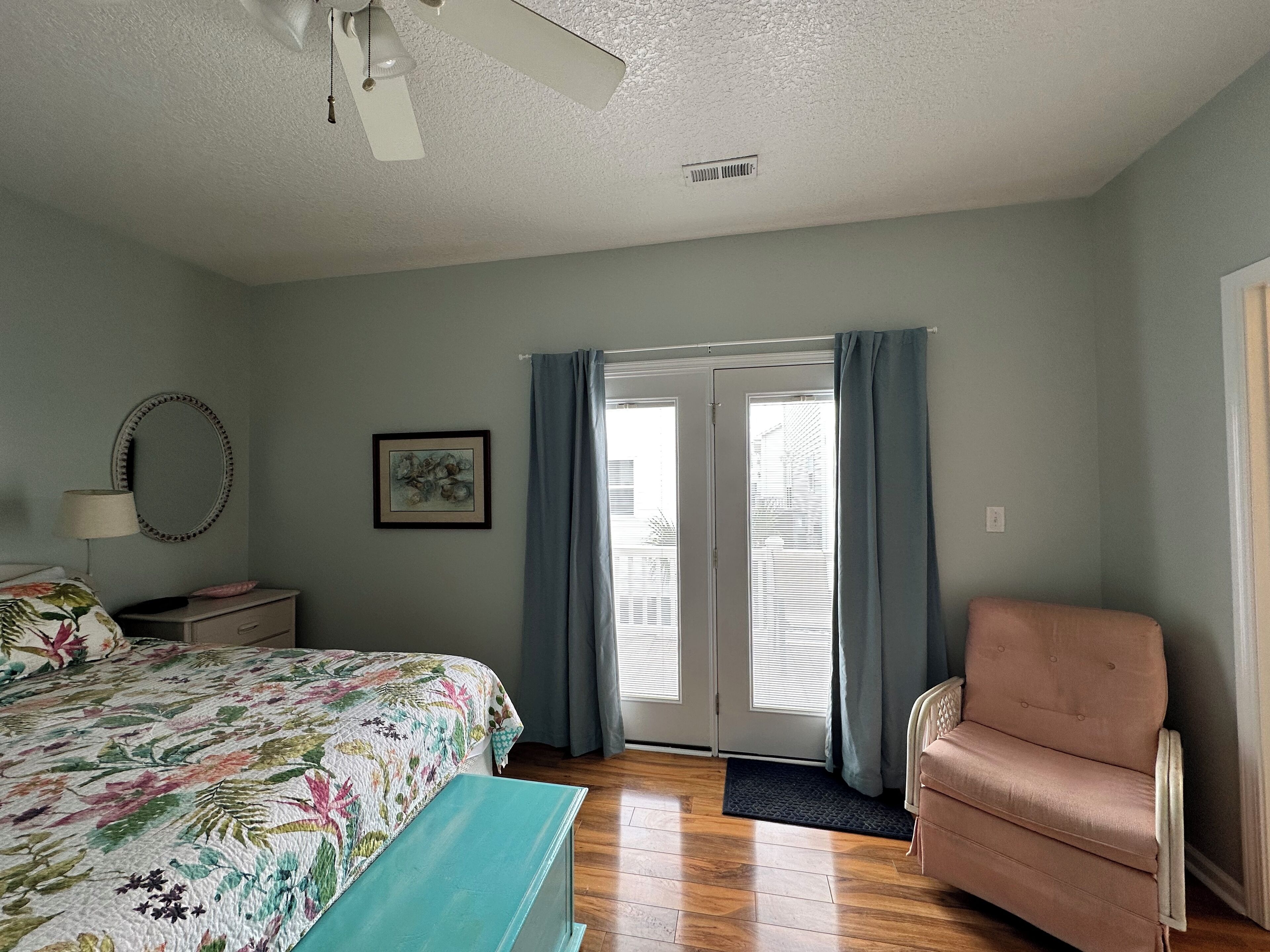 A bedroom with a bed, a chair, a dresser, a mirror, and a door with curtains.