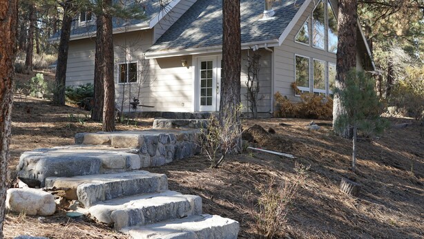 Une maison avec un escalier en pierre menant à la porte d’entrée, entourée d’arbres et d’un mur en pierre.