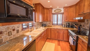 A kitchen with wooden cabinets, a stainless steel microwave, a double sink, and a tiled backsplash. - Spacious ski in double condo prime base area location by Mountaineer Square.   (Mt. Crested Butte)