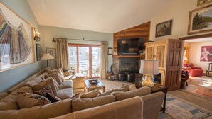 A cozy living room with a sofa, a fireplace, a television, and a large window with curtains. - Spacious ski in double condo prime base area location by Mountaineer Square.   (Mt. Crested Butte)