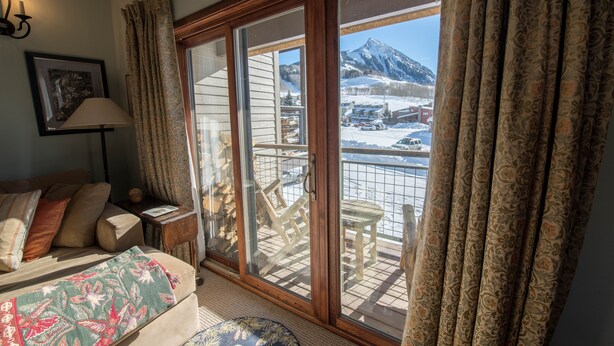 A cozy room with a sofa, a lamp, and a view of a snowy mountain through a sliding glass door. - Spacious ski in double condo prime base area location by Mountaineer Square.   (Mt. Crested Butte)