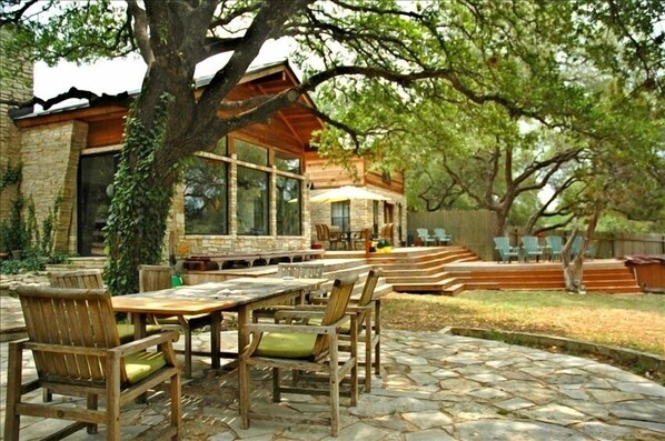 A patio area with a stone table and chairs, a wooden pergola, and a stone building with large windows.
