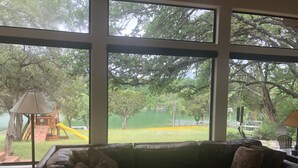 A room with a large window overlooking a playground and a lake. - Austin Lake Travis Pool Waterfront -  Hill Country Retreat 2 Acres  Sleeps 20 (Leander)
