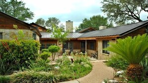 A modern house with a stone facade, a metal roof, and a landscaped garden with various plants and a pathway. - Austin Lake Travis Pool Waterfront -  Hill Country Retreat 2 Acres  Sleeps 20 (Leander)
