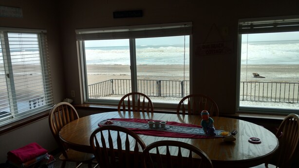 Un comedor con mesa y sillas, ventanas amplias con vista a la playa y al océano, y un cartel que dice "Welcome To The Beach".