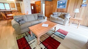 Uma sala de estar com sofá, duas poltronas, uma mesa de centro de madeira e um tapete.