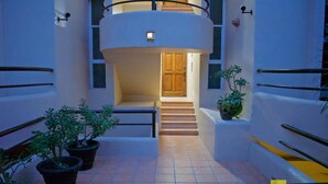 Un bâtiment moderne avec un escalier central menant à une porte en bois, entourée de plantes en pot et de rampes de protection en métal.