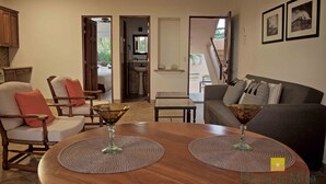 Un salon avec une table ronde en bois, deux fauteuils, un canapé et, au fond, un coin cuisine.