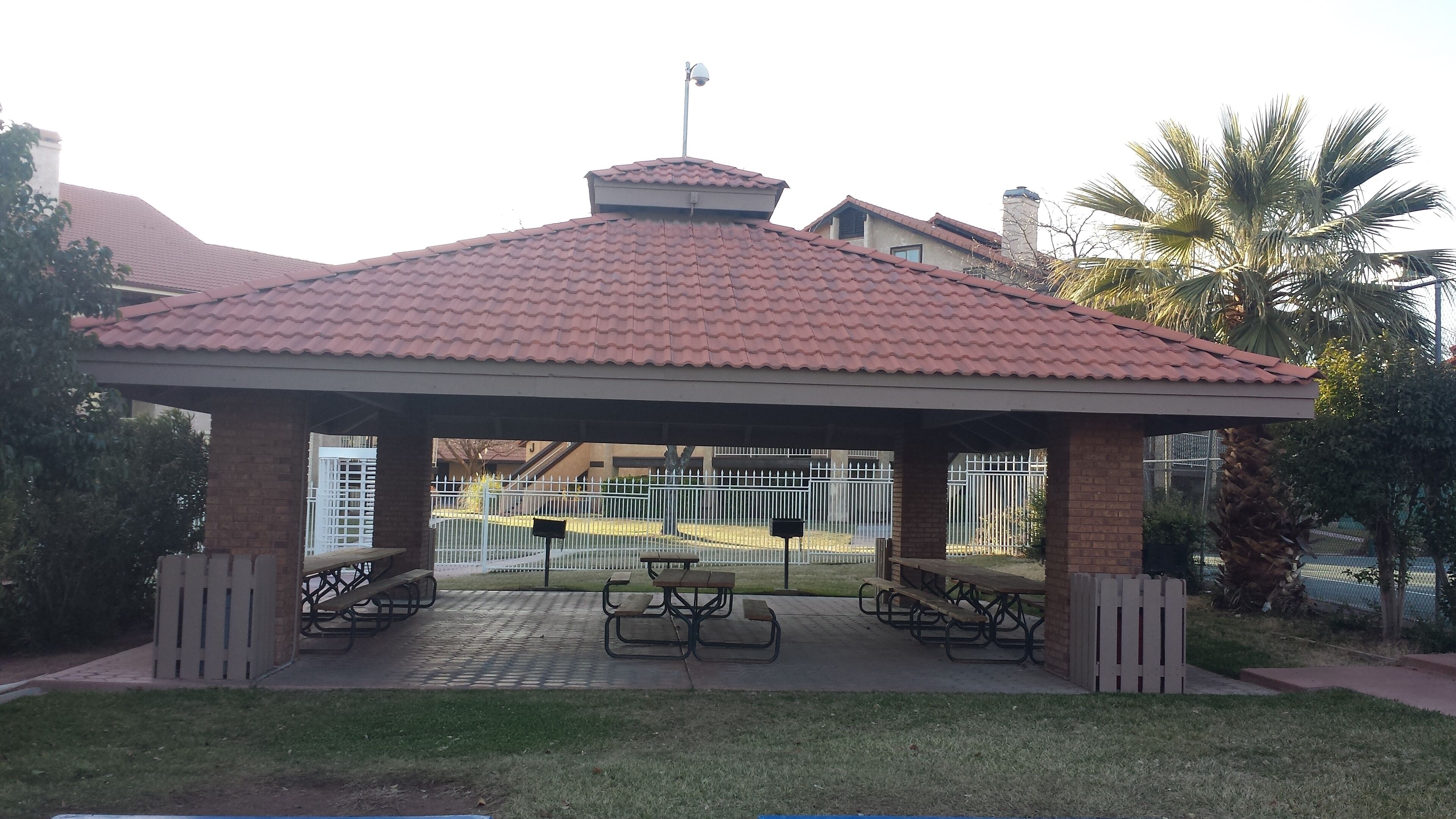 A covered pavilion with a tiled roof, benches, and a fenced area.