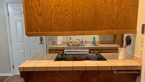 Cozinha com bancada de madeira, três banquetas vermelhas, uma pia e um armário de madeira acima da bancada.