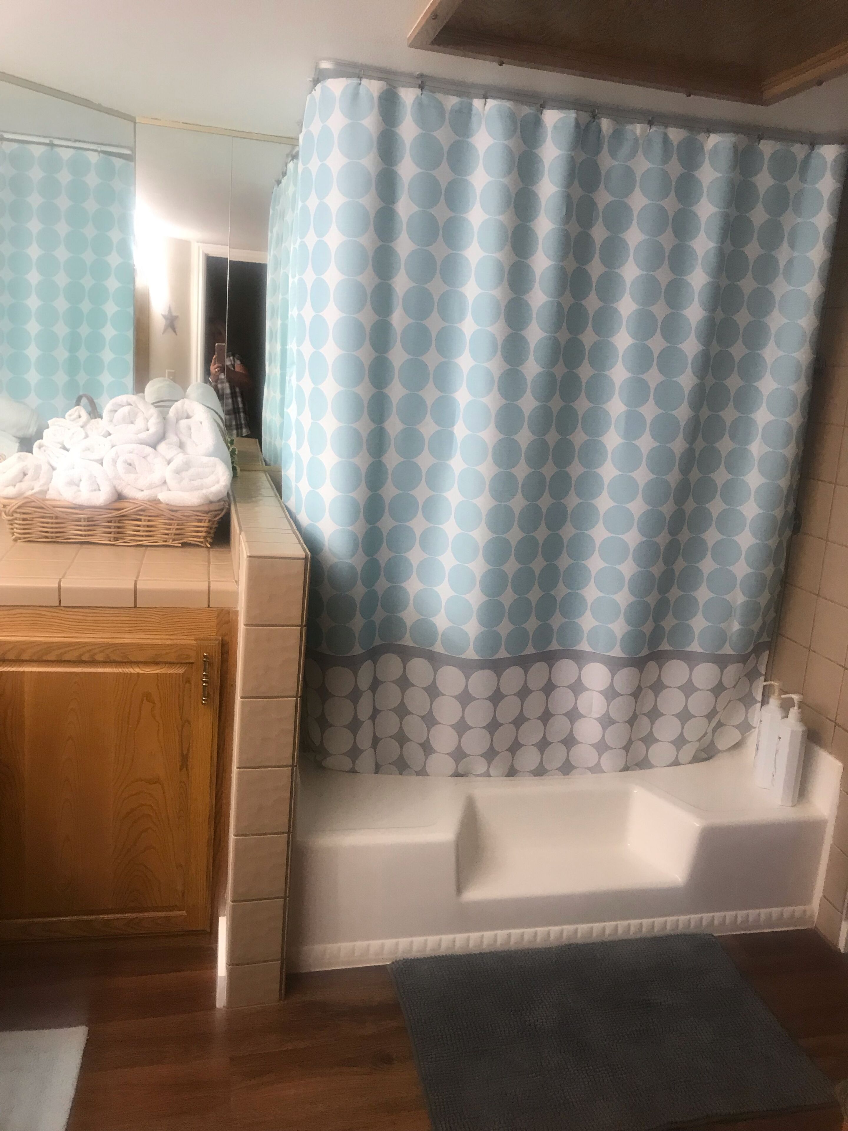 Een badkamer met een badkuip, een houten kastje, een rieten mand met handdoeken en een douchegordijn met een cirkelpatroon.
