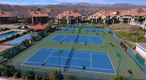 Complejo de canchas de tenis al aire libre con varias canchas, rodeado de edificios residenciales y una piscina.