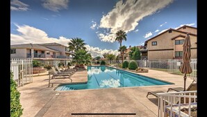 Piscina com espreguiçadeiras, cerca branca e casas ao fundo.