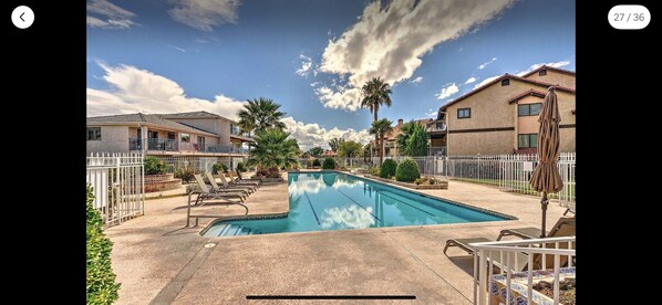 Una piscina con sillones de descanso, una valla blanca y casas al fondo.