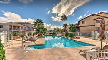 A swimming pool with lounge chairs, a white fence, and houses in the background.