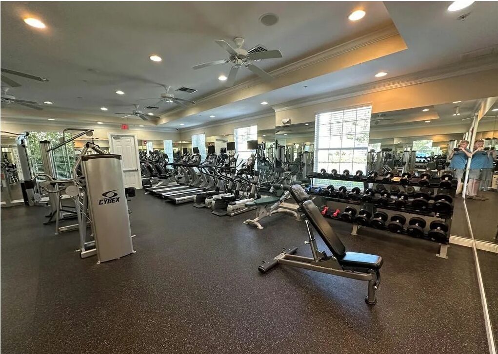 A gym with various exercise equipment, mirrors, and a ceiling fan.