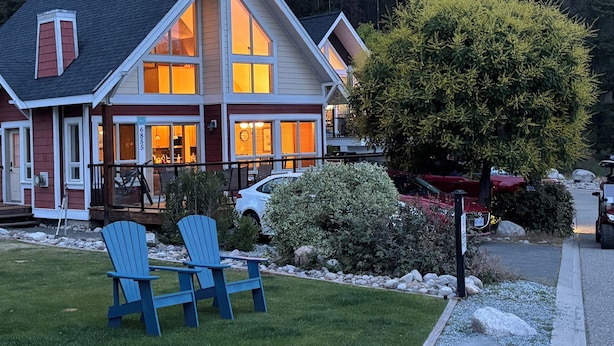 A two-story house with a porch, a dining area, and a large tree in the yard. - Amazing unobstructed Lake Okanagan view - Booking for summer 2026 now! (Kelowna)