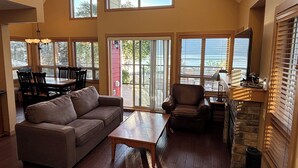 A spacious living room with a high ceiling, large windows, a fireplace, and a dining area. - Amazing unobstructed Lake Okanagan view - Booking for summer 2026 now! (Kelowna)