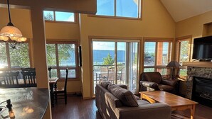 A spacious living area with a sofa, coffee table, and a fireplace. There are large windows offering a view of the outdoors. - Amazing unobstructed Lake Okanagan view - Booking for summer 2026 now! (Kelowna)