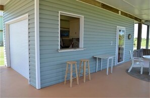 A covered porch with a table and two stools, a window, and a door.