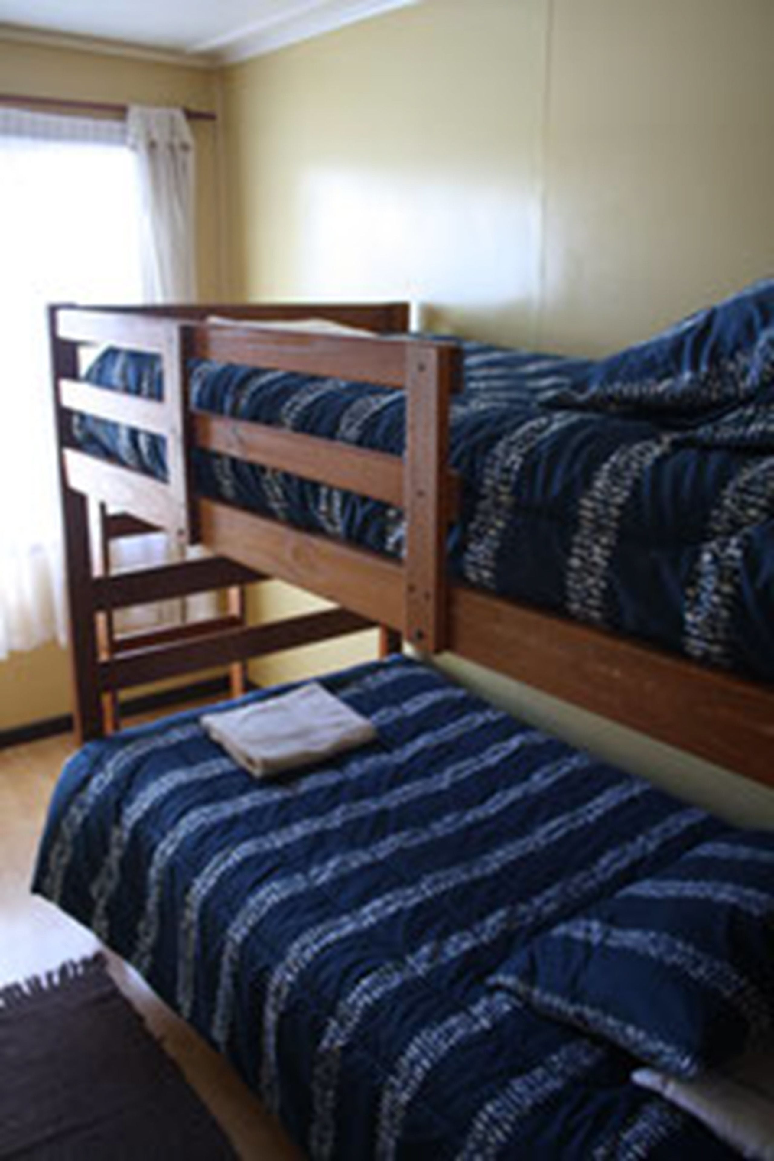 Una cama individual con estructura de madera y colcha azul estampada.