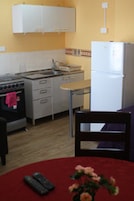 Una cocina funcional con estufa, horno, lavaplatos y refrigerador. Hay una mesa de comedor con dos sillas y un florero con flores.