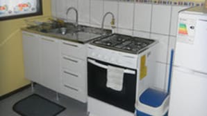 Una cocina con gabinetes blancos, estufa, pileta y refrigerador.