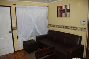 Una habitación con un sofá de cuero marrón, una cortina blanca y un panel eléctrico instalado en la pared.