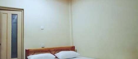 Una cama individual con cabecera de madera, ropa de cama blanca y una mesita de noche pequeña con una lámpara.
