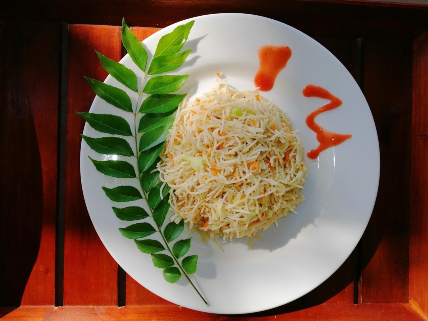 A plate of shredded vegetables with a decorative leaf and a drizzle of sauce.