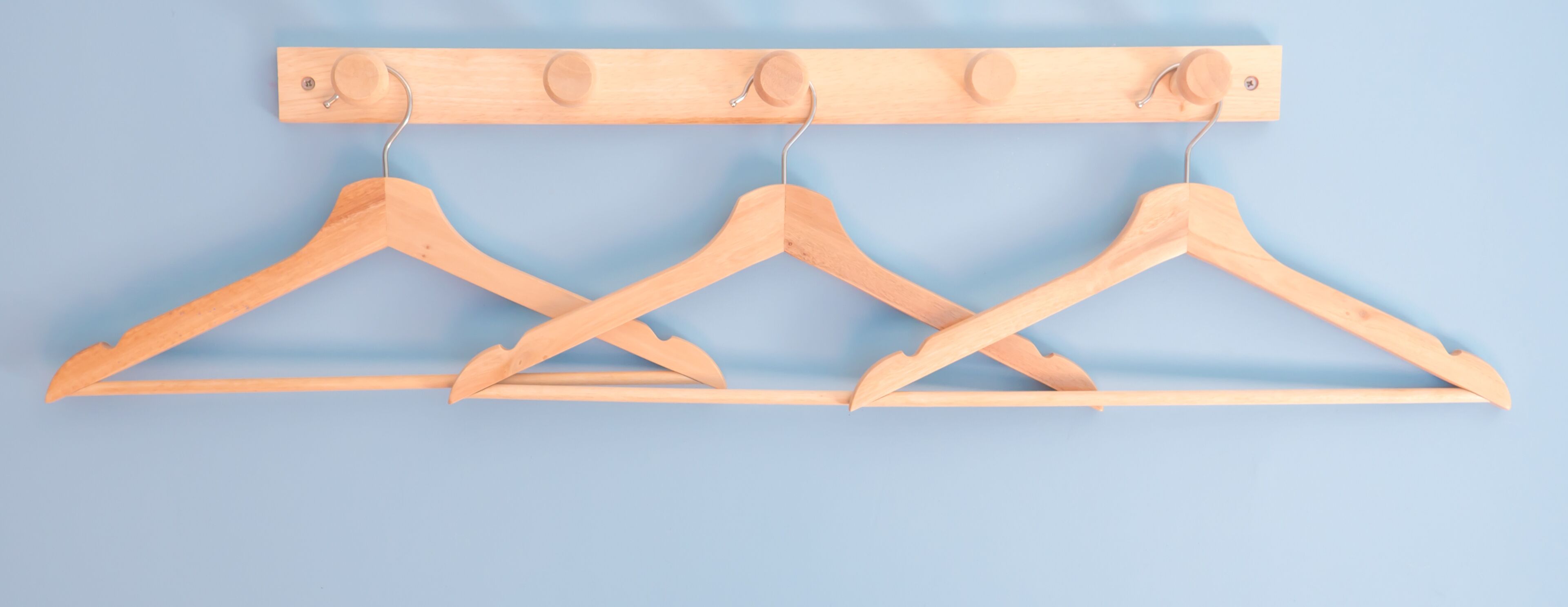 Three wooden hangers on a wooden rack against a blue background.