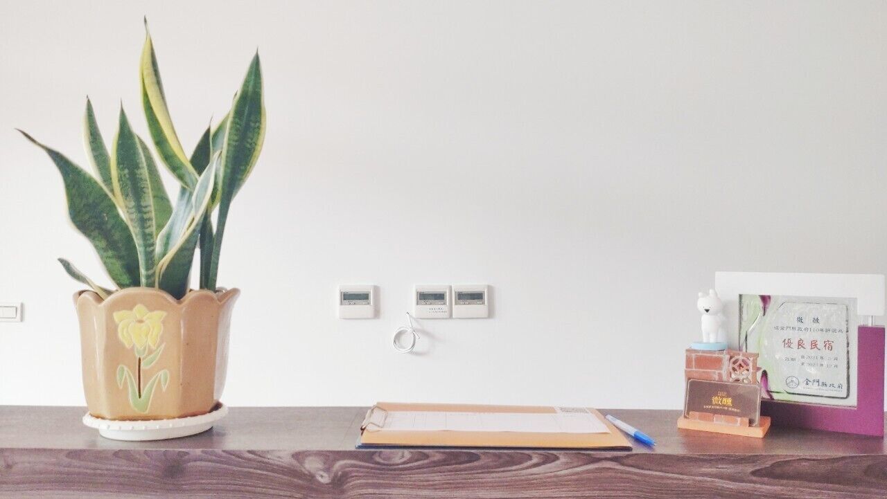 A desk with a potted plant, a notepad, a pen, a small bottle, and a card.