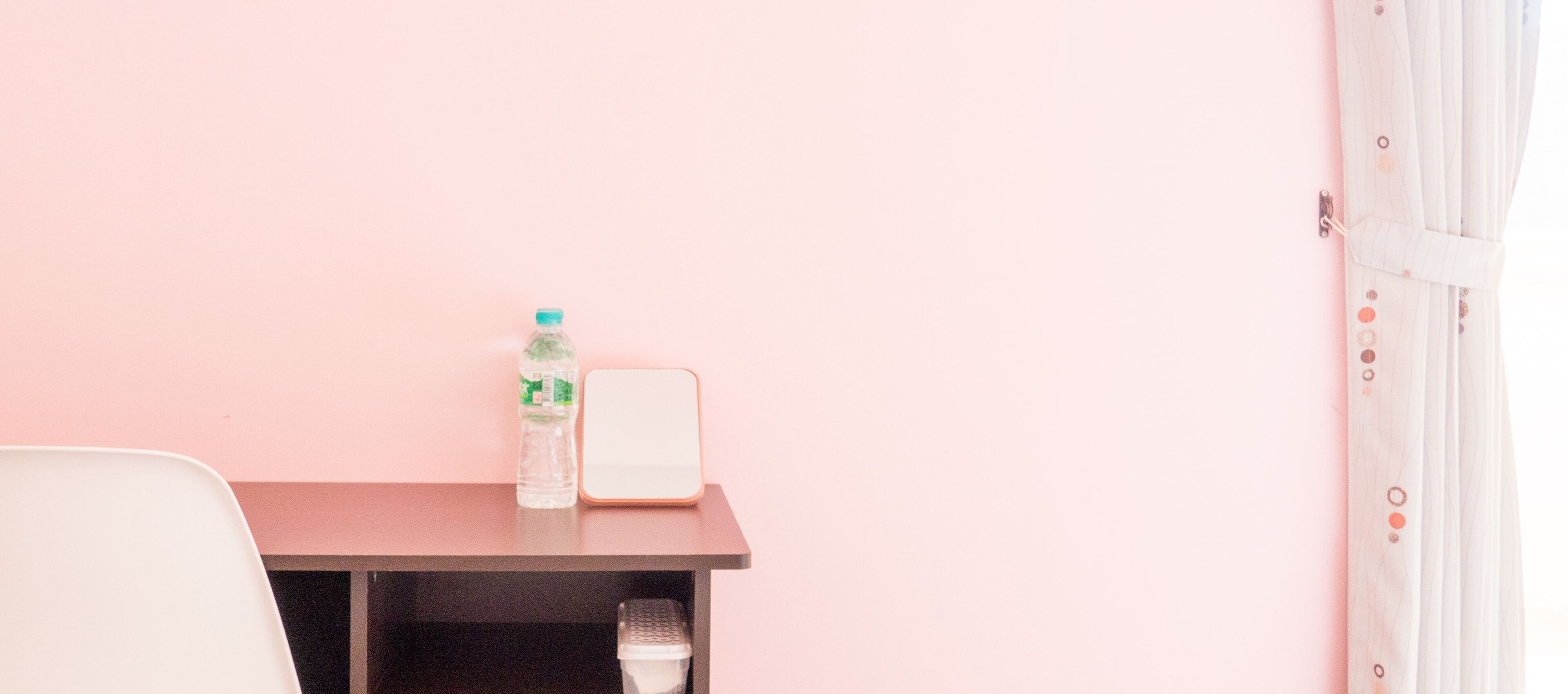 A small table with a water bottle and a white device, possibly a speaker, against a pink wall.