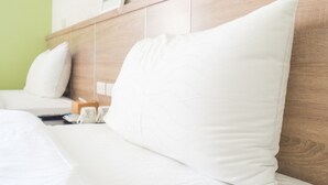 Una cama con ropa de cama y almohadas blancas, un cabecero de madera y una mesita de noche con un control remoto y una caja de pañuelos.