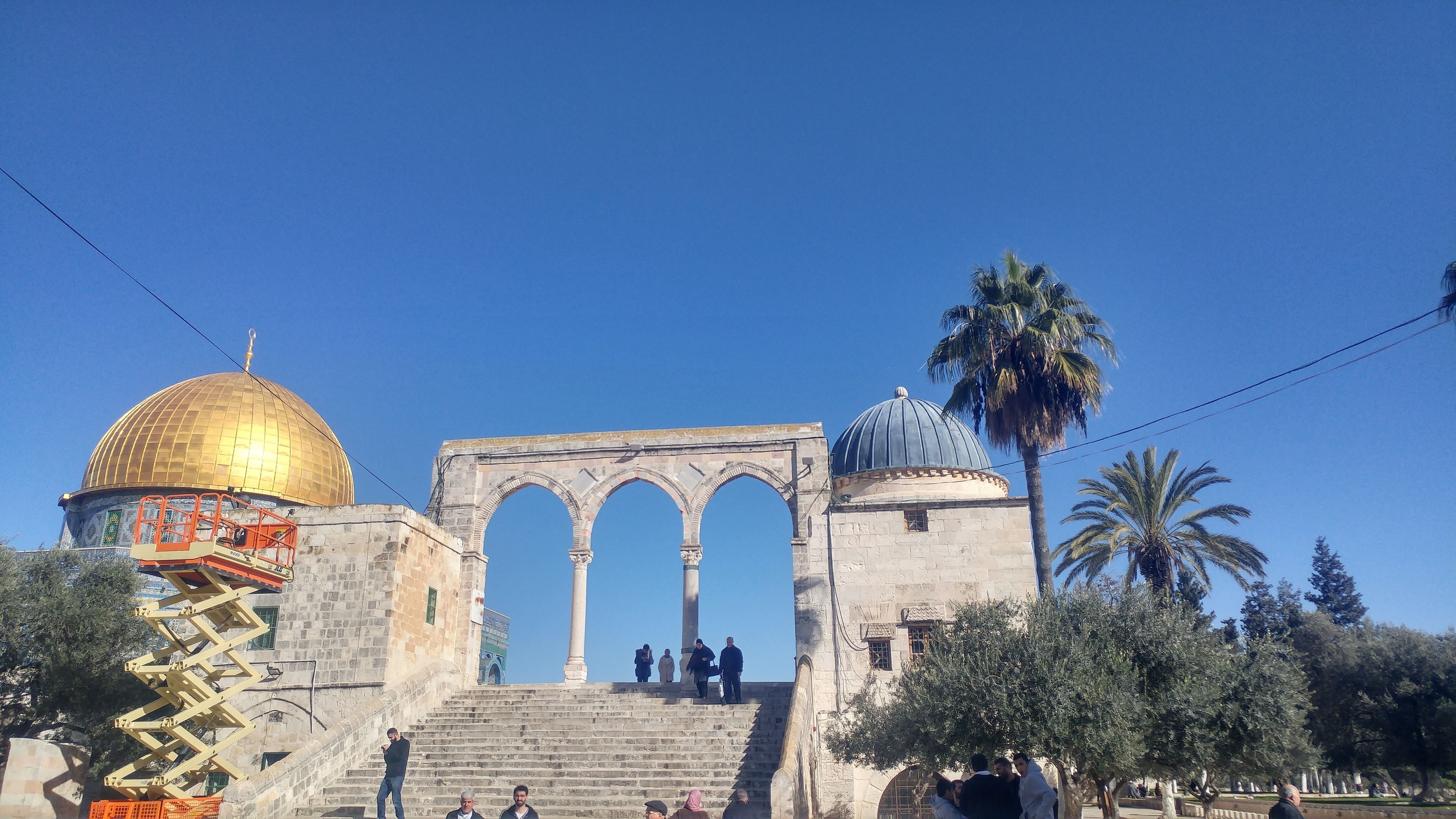 A historical site with a golden dome, a large archway, and a staircase leading up to it.