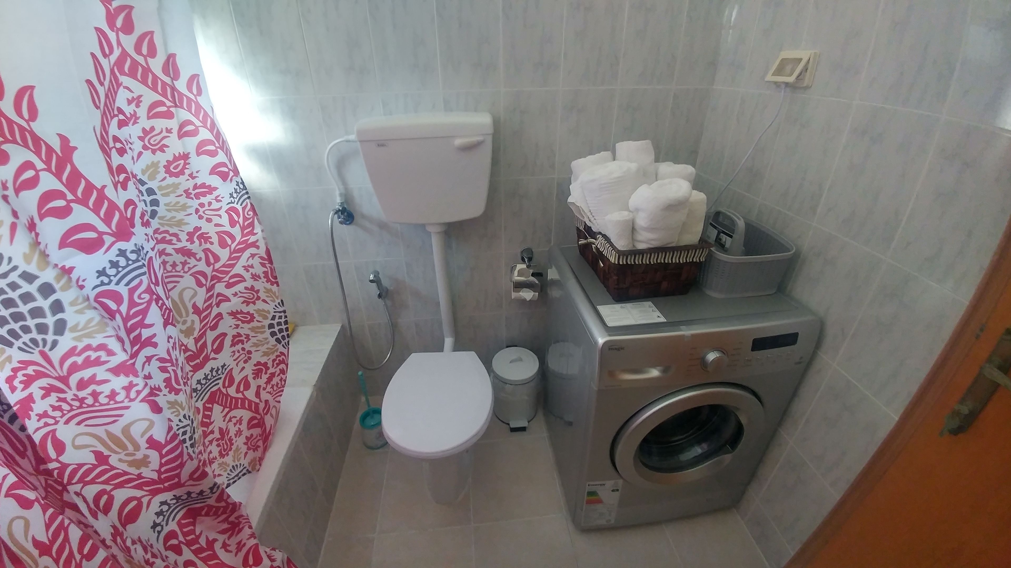 A compact bathroom with a toilet, washing machine, and a shower area.
