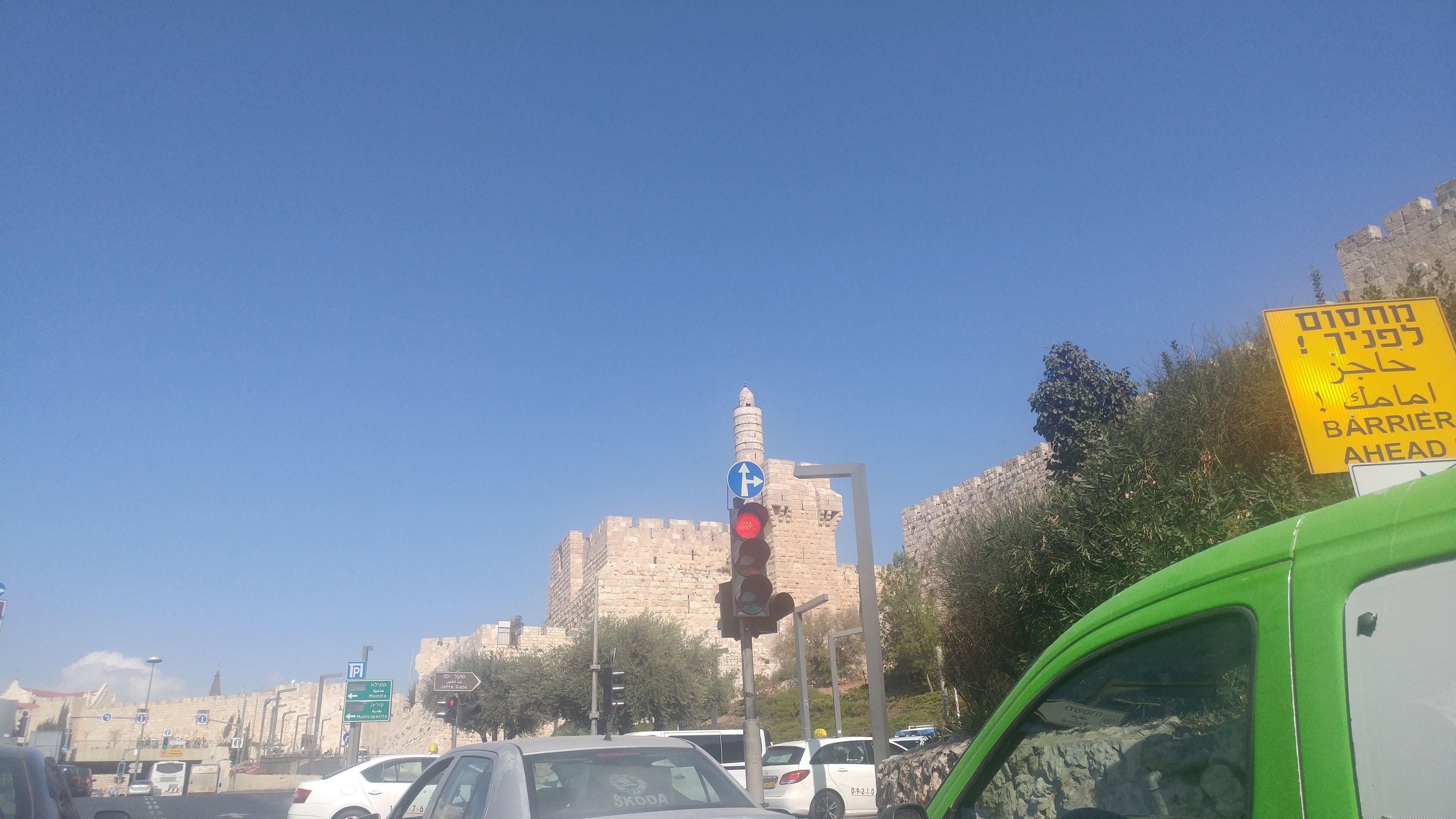 A busy street with traffic lights, a green van, and a historic stone wall in the background.