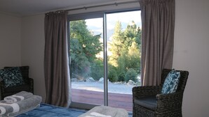 A room with a bed, two wicker chairs, a large window with curtains, and a view of trees and mountains. - Alpine Views Burkes Pass (Burkes Pass)