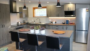 A modern kitchen with a central island, black bar stools, stainless steel appliances, and pendant lighting. - Alpine Views Burkes Pass (Burkes Pass)