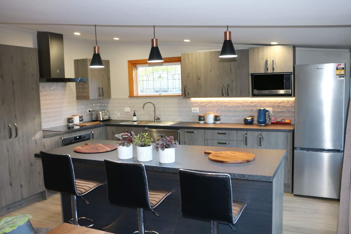 A modern kitchen with a central island, black bar stools, stainless steel appliances, and pendant lighting.