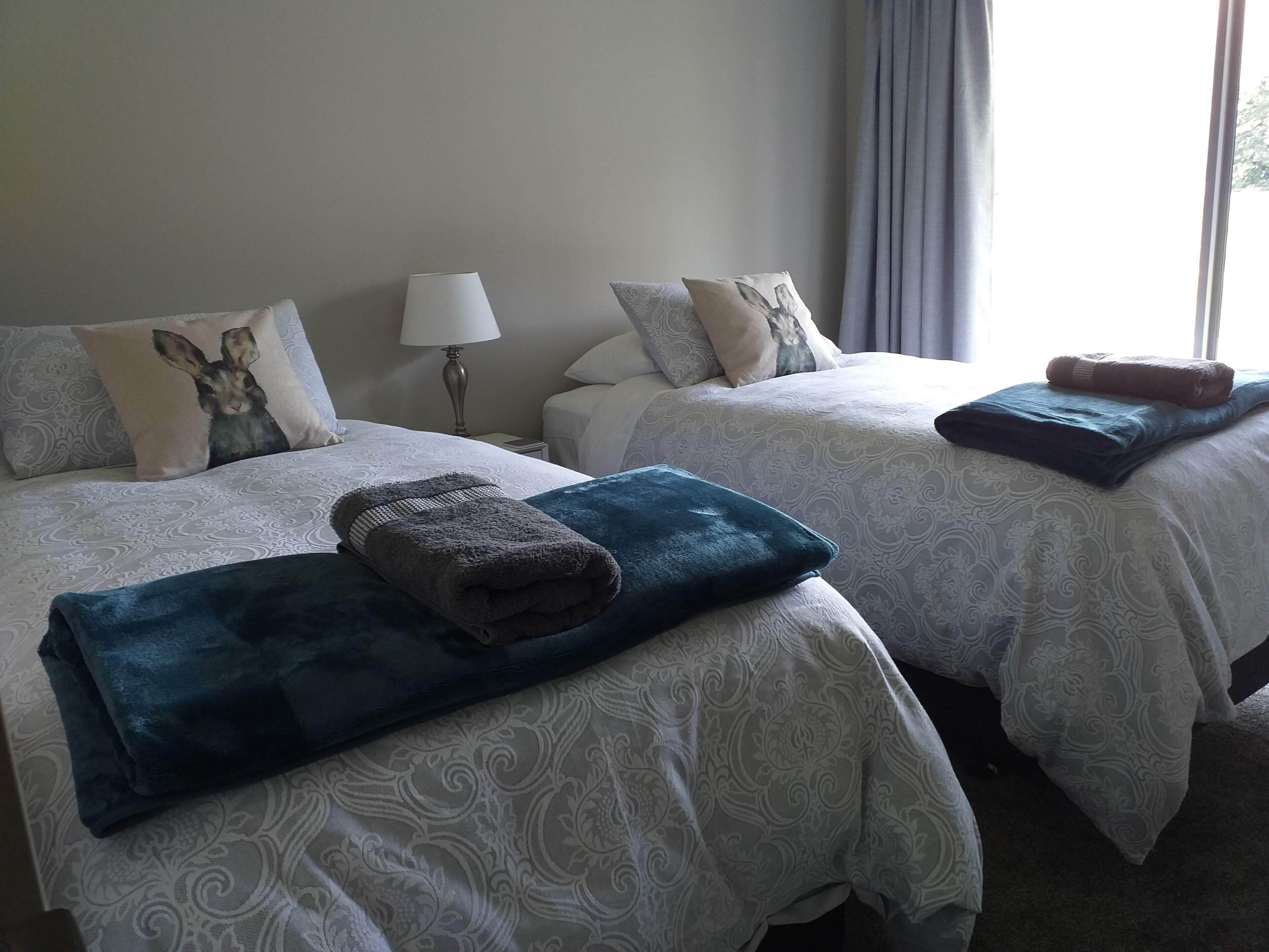 Dos camas con ropa de cama estampada, una lámpara y una ventana con cortinas.